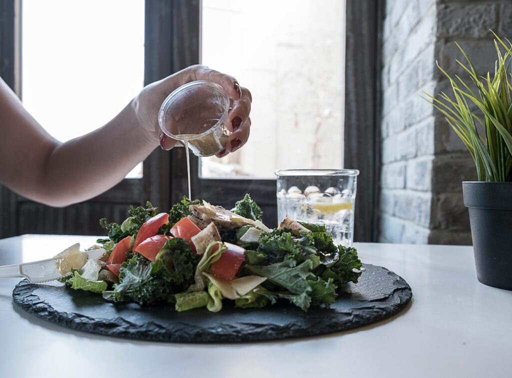 pexels-photo-1332313-1332313 Hand pouring dressing over fresh salad with kale and tomatoes in a modern Dubai restaurant.